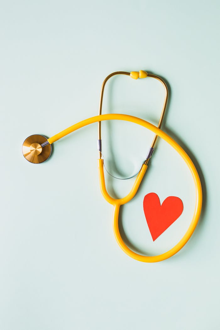 Product Yellow stethoscope arranged with a red heart cutout on a light green background, symbolizing heart health.
